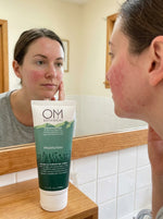 Woman applying OM Botanicals moisturizer to her face in front of a mirror.