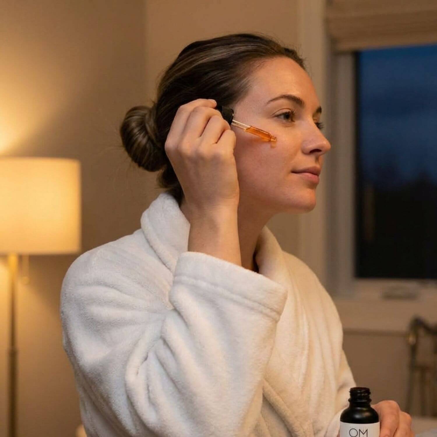 Woman applying a dropper of OM Botanical Bakuchiol Serum to her face in a room setting.